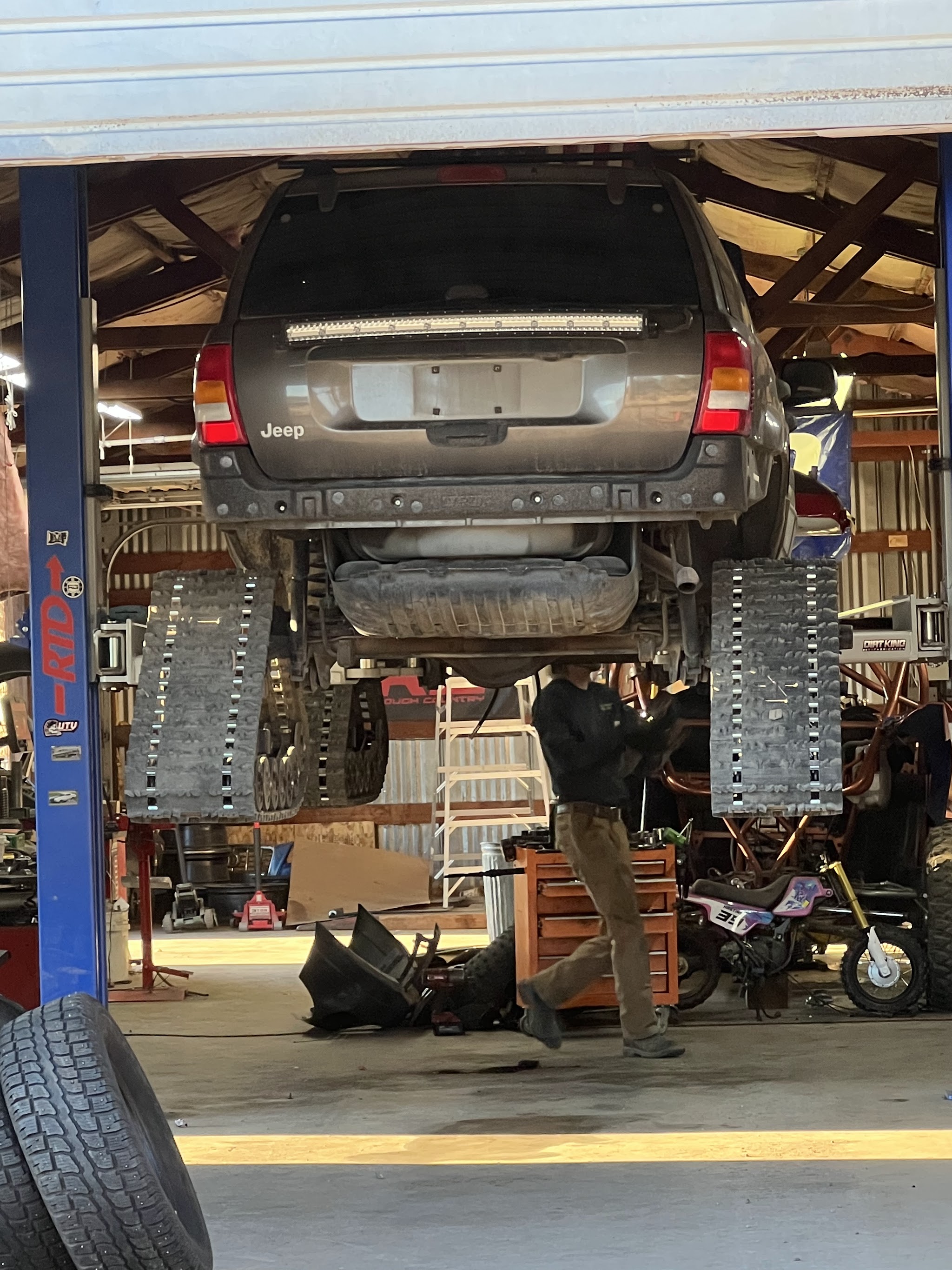 A Jeep up on the hoist with work going on underneath at Hastings Tire & Offroad